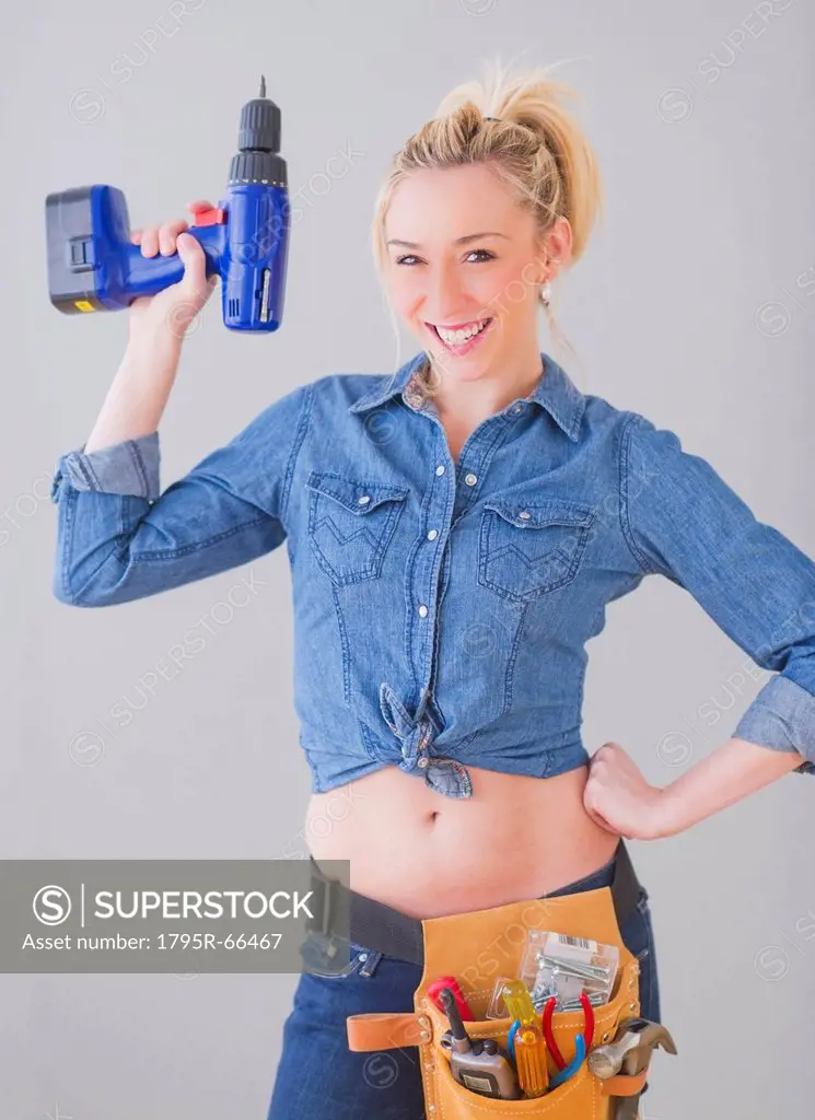 Portrait of young woman wearing tool belt and holding drill, studio shot