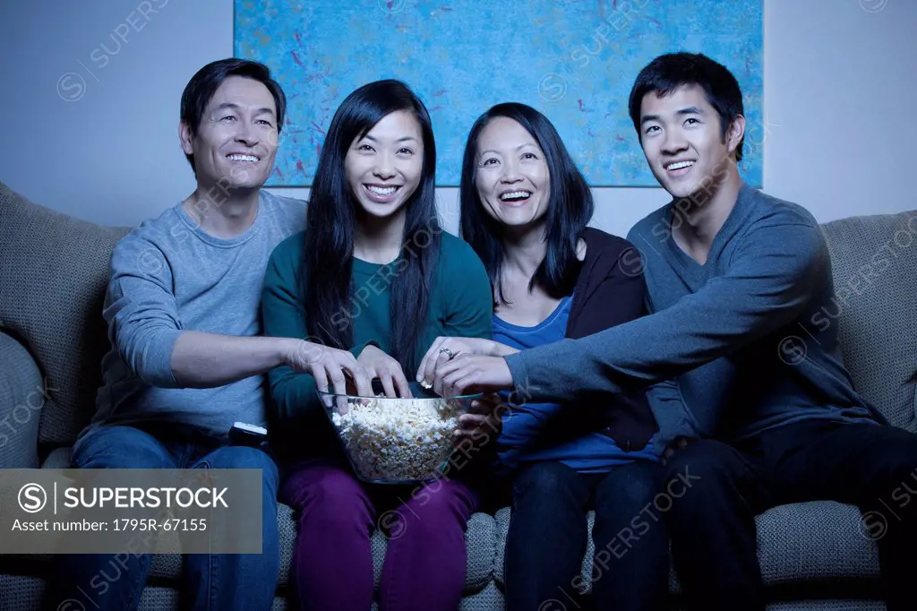 Smiling family watching TV and eating popcorn