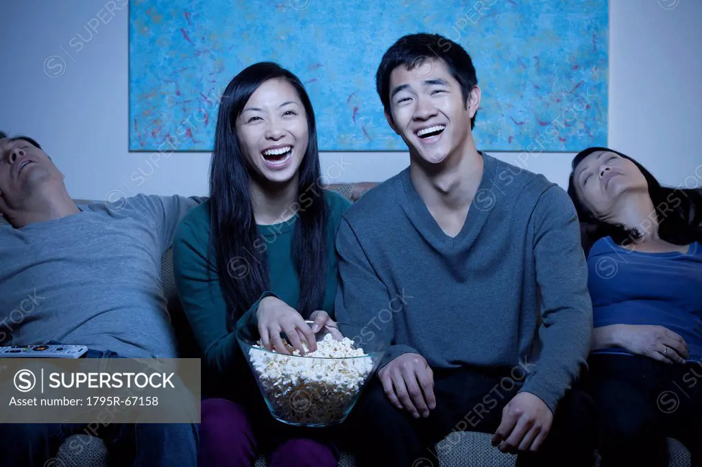 Smiling family watching TV and eating popcorn
