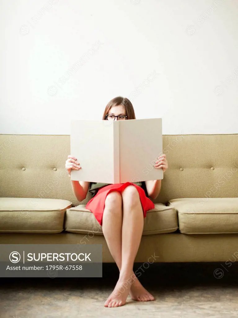 Young woman sitting on sofa with book