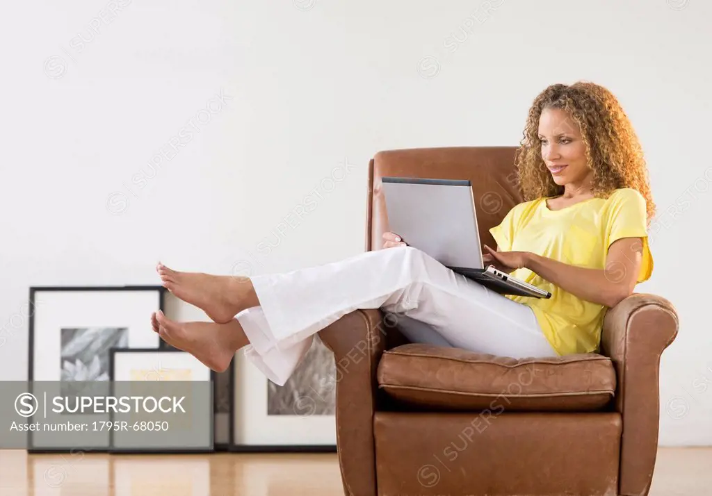Woman sitting in armchair using laptop