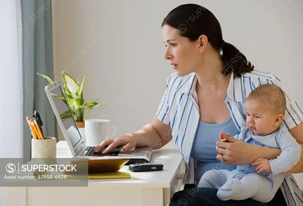 Mother typing on laptop and holding baby