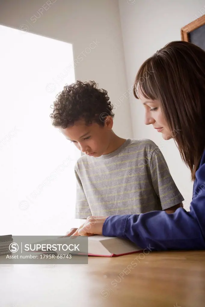 Schoolboy reading with teacher in classroom