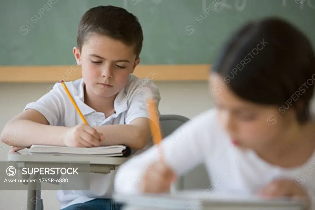 Boy writing at desk in classroom
