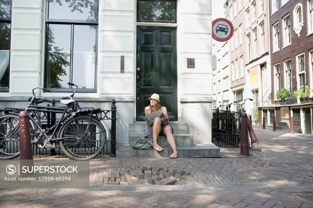 Holland, Amsterdam, Female tourist with map sitting on steps