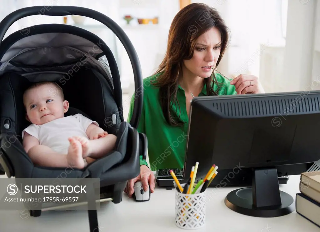 Mother working on computer, baby daughter 6_11 months on desk