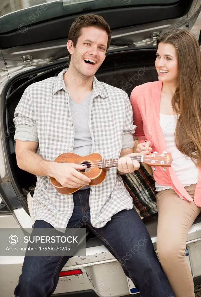 Happy young couple sitting in car boot with mandolin