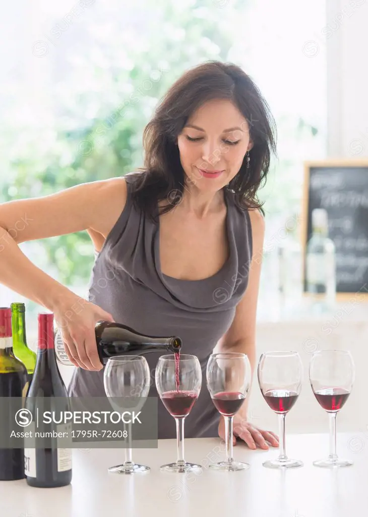 Woman purring red wine into wine glasses