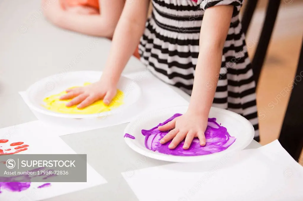 Girl 4_5 holding her hands on plates with paint