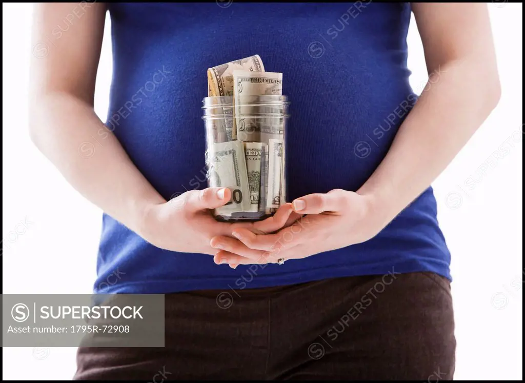 Studio Shot of mid section of pregnant woman holing jar with money