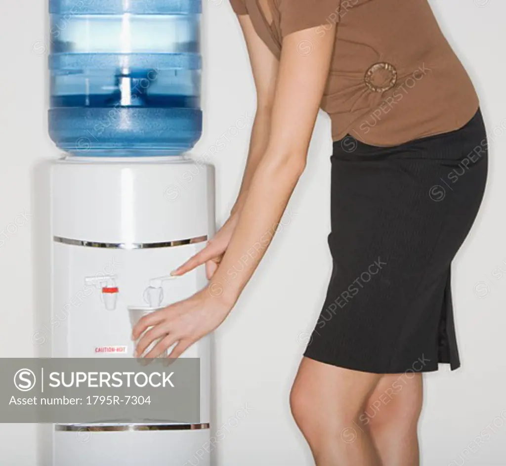 Businesswoman filling cup at water cooler