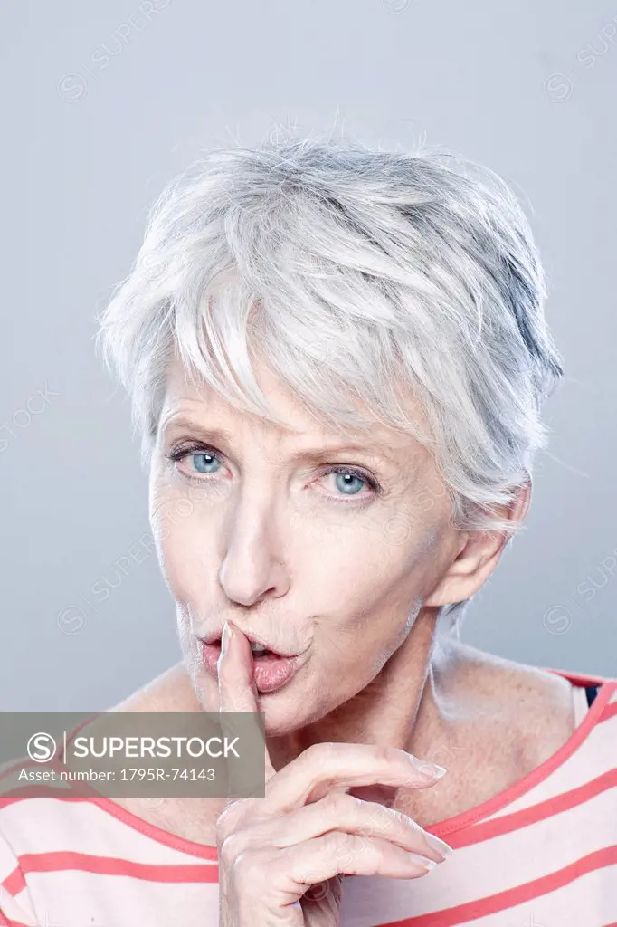Portrait of senior woman with finger on her lips, studio shot