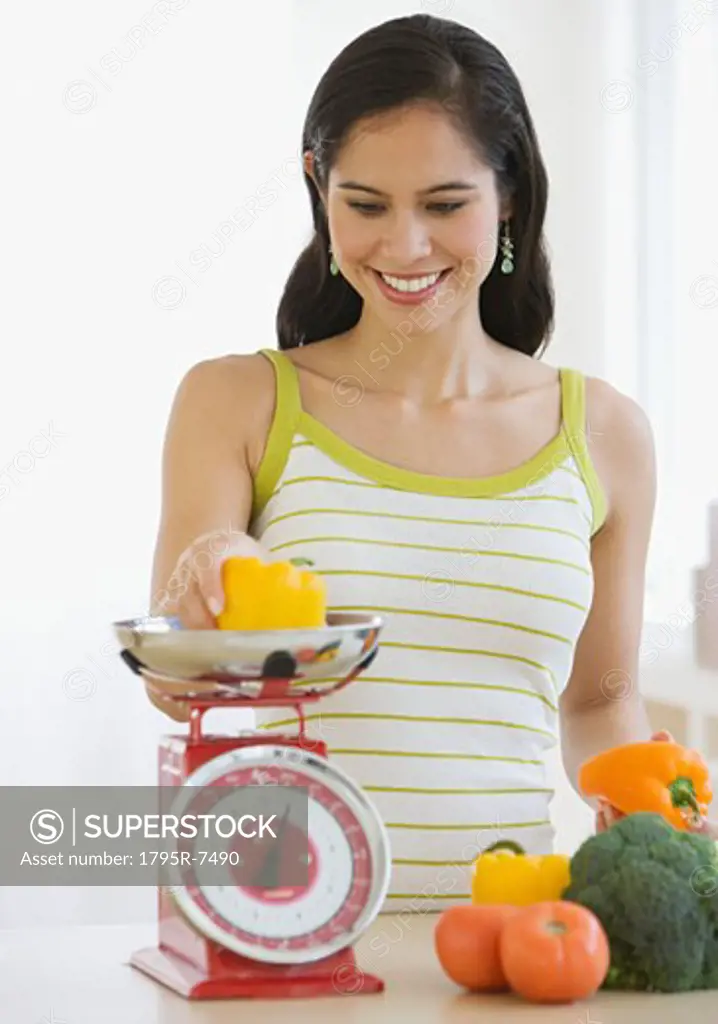 Woman weighing vegetables in kitchen
