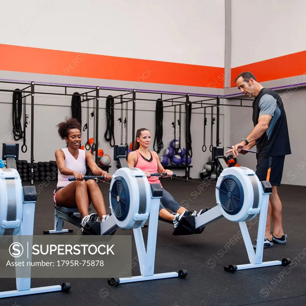 Two women exercising in gym supervised by their trainer