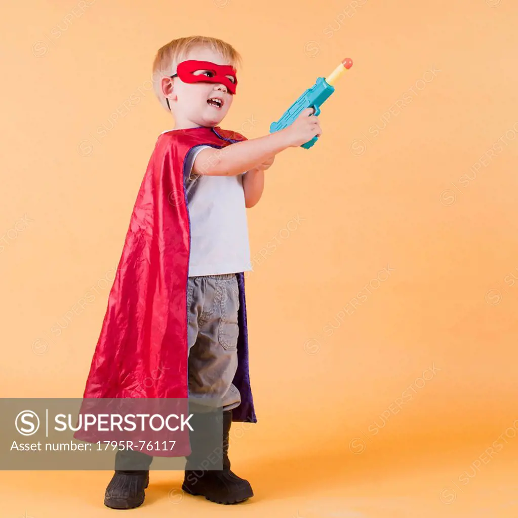 Studio shot, Portrait of boy 2_5 years wearing cape and holding toy gun