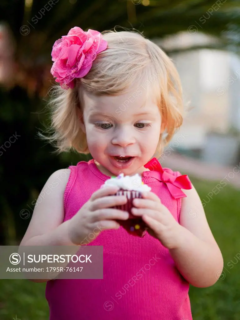 Girl with blong hair looking at cupcake
