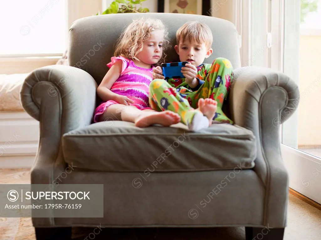 Girl and boy sitting on armchair and playing video game