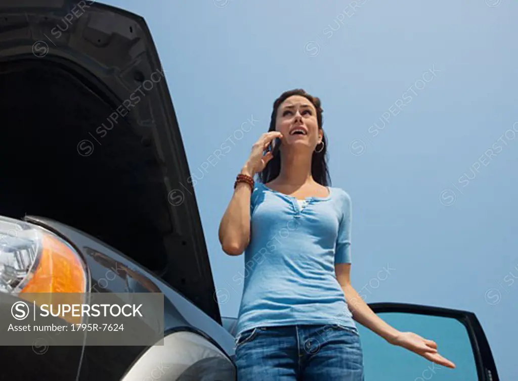 Woman talking on cell phone next to broken down car