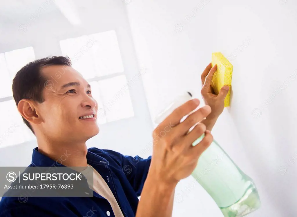 Man washing white walls with spray and yellow sponge