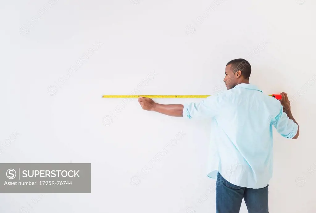 Young man measuring white wall