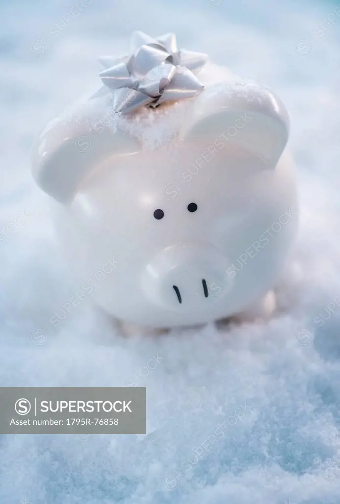 Studio shot of white piggy bank with gift bow on artificial snow
