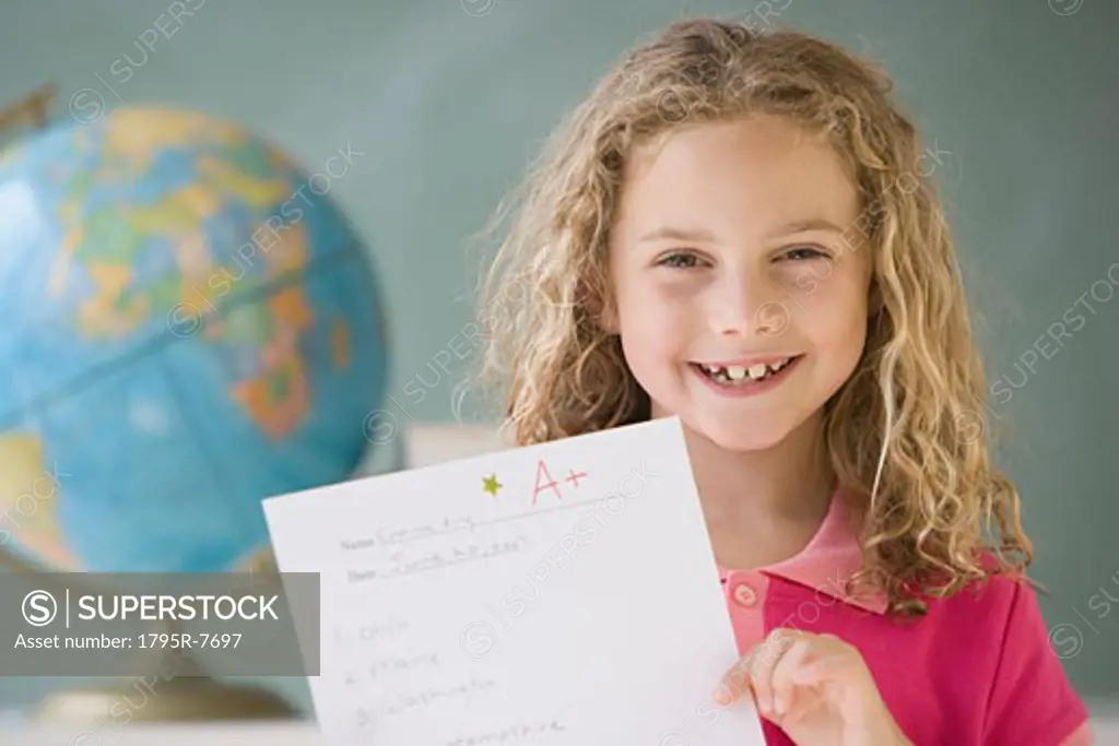Girl holding up A plus paper in classroom