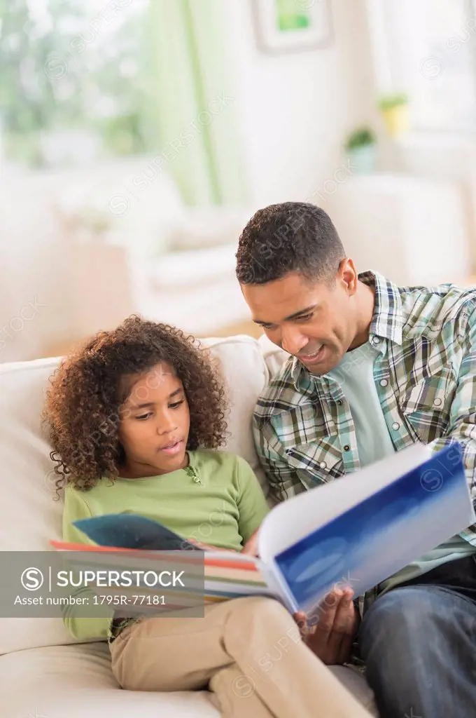 Father with daughter 6_7 reading book on sofa