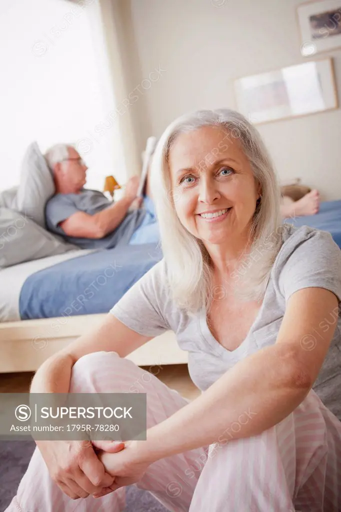 Portrait of senior woman, man sitting on bed in background