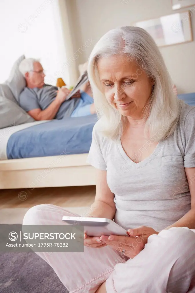 Senior woman holding photo frame, man sitting on bed in background