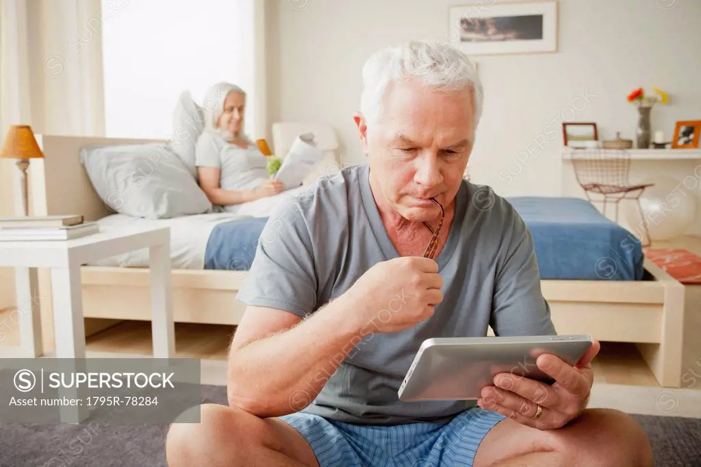 Senior man holding photo frame, woman sitting on bed in background
