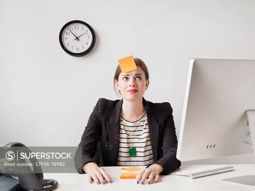 Studio shot of young woman working in office with adhesive note on her forehead
