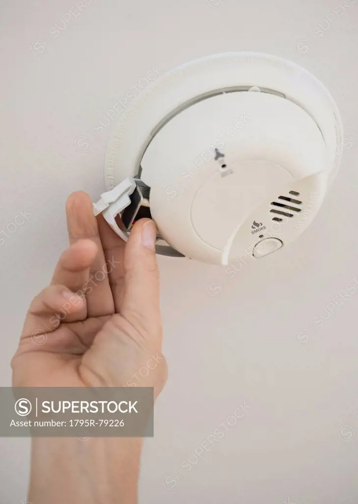 Hand changing battery in smoke alarm