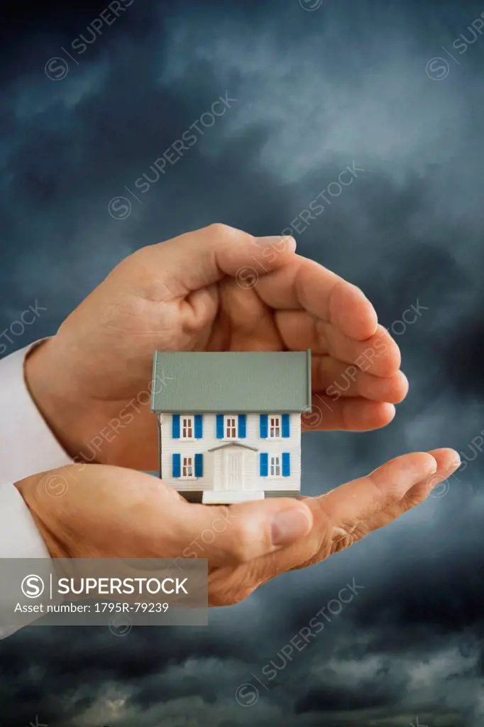 Hands holding model house in front of stormy sky