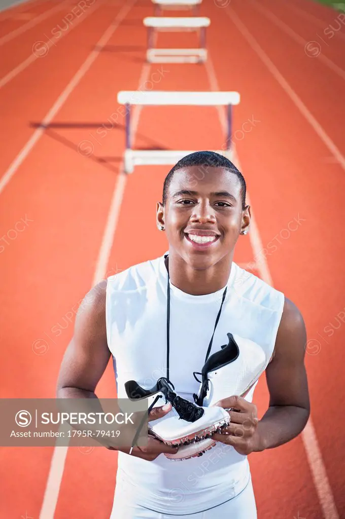 Portrait of smiling boy 12_13 leaning on hurdle on running track