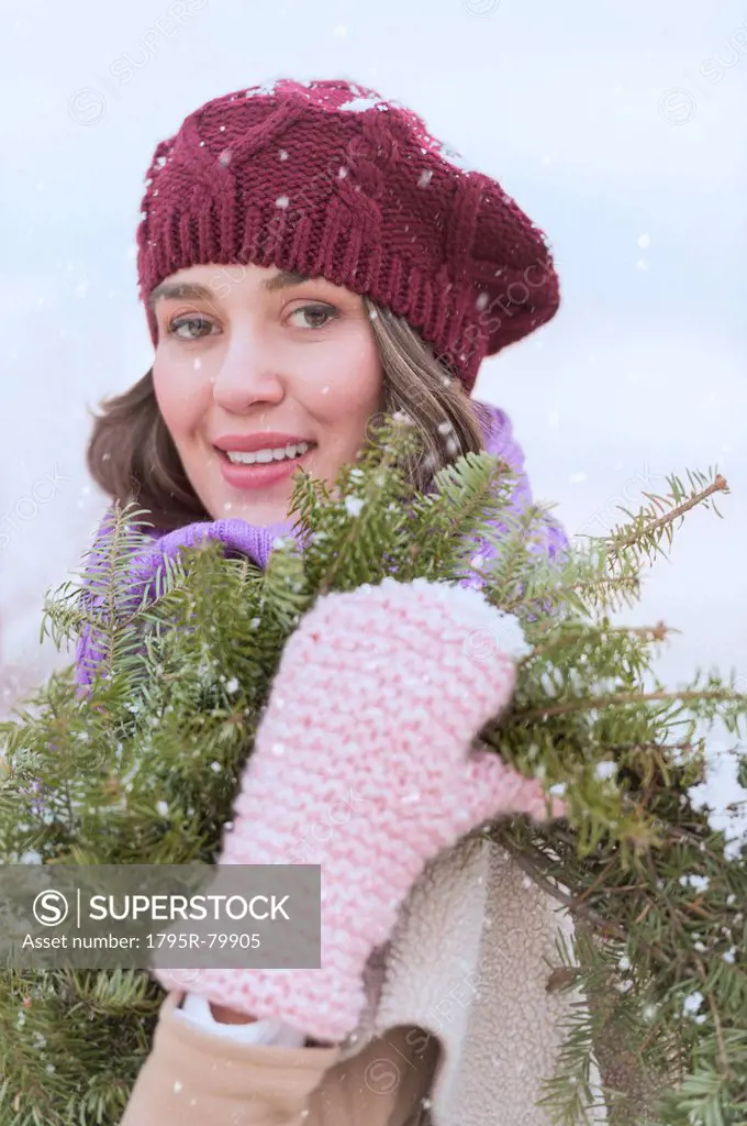 Portrait of young woman wearing knit hat, gloves and scarf an carrying fir wreath
