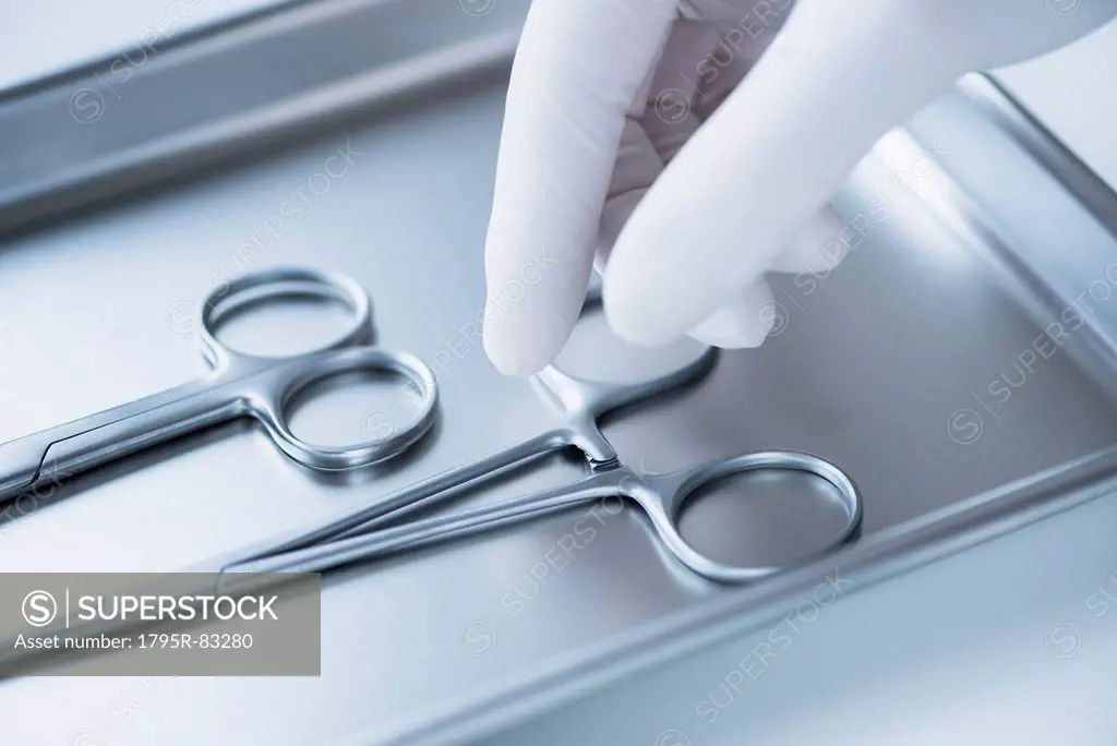 Close up of hand in surgical glove choosing dental forceps, studio shot