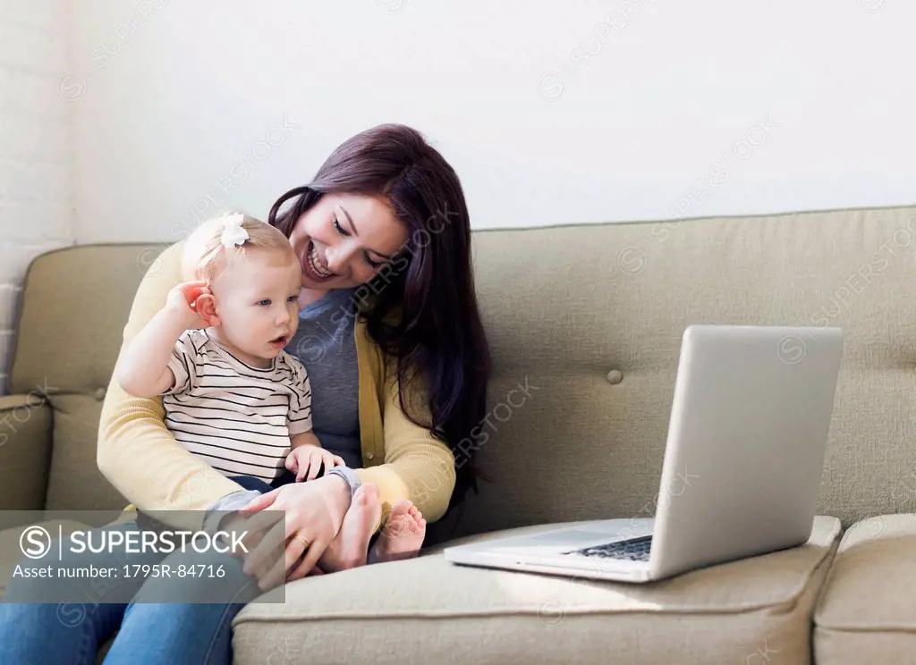 Woman and baby girl (12-17 months) sitting on sofa and using laptop