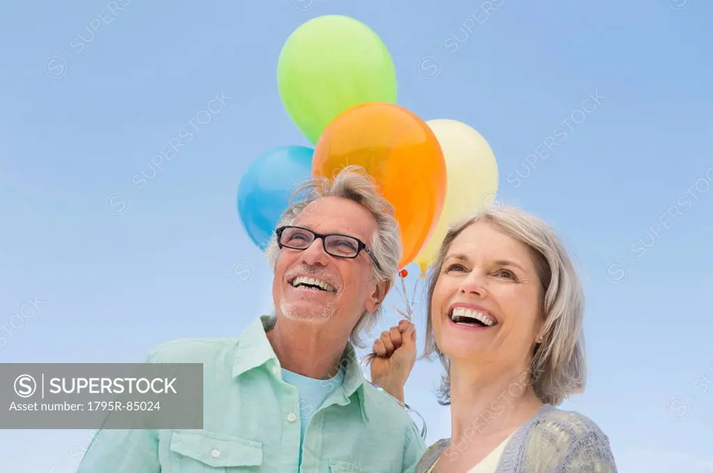Senior couple with bunch of balloons against clear sky