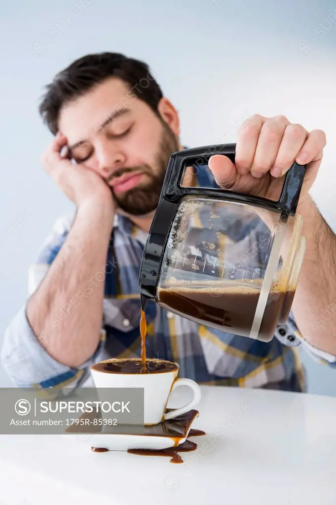 Tired, sleepy man spilling coffee on table