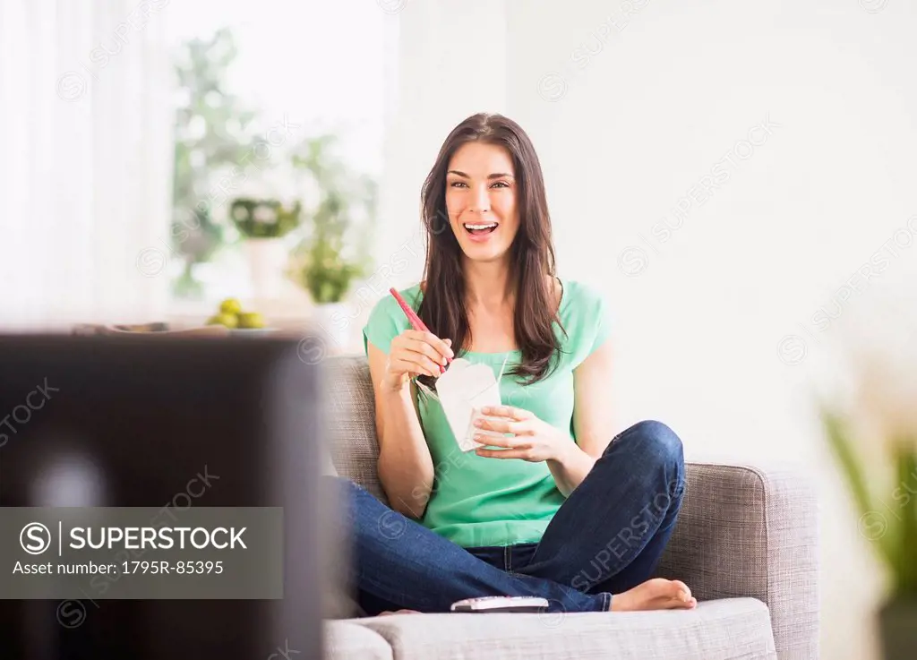 Portrait of woman watching tv and eating take out food