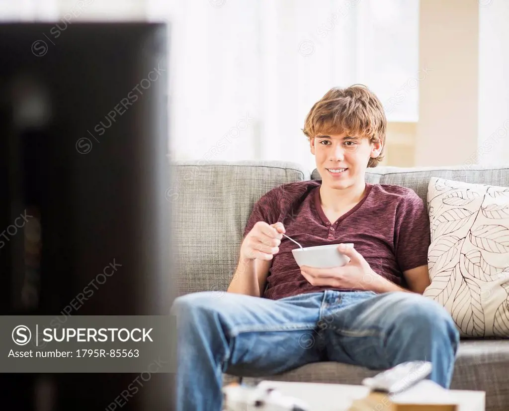 Teenage boy (14-15) watching tv and eating