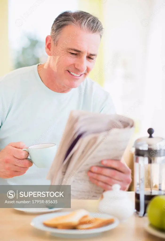 Portrait of man reading newspaper and having breakfast