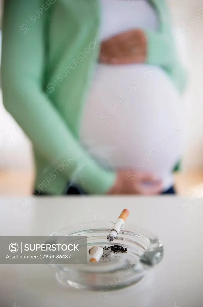 Mid section of pregnant woman, ashtray and cigarette in front