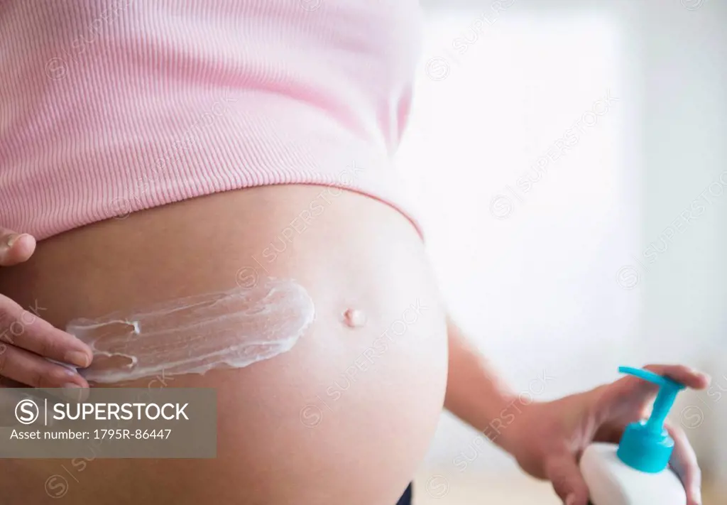 Mid section of pregnant woman applying moisturizer on her belly
