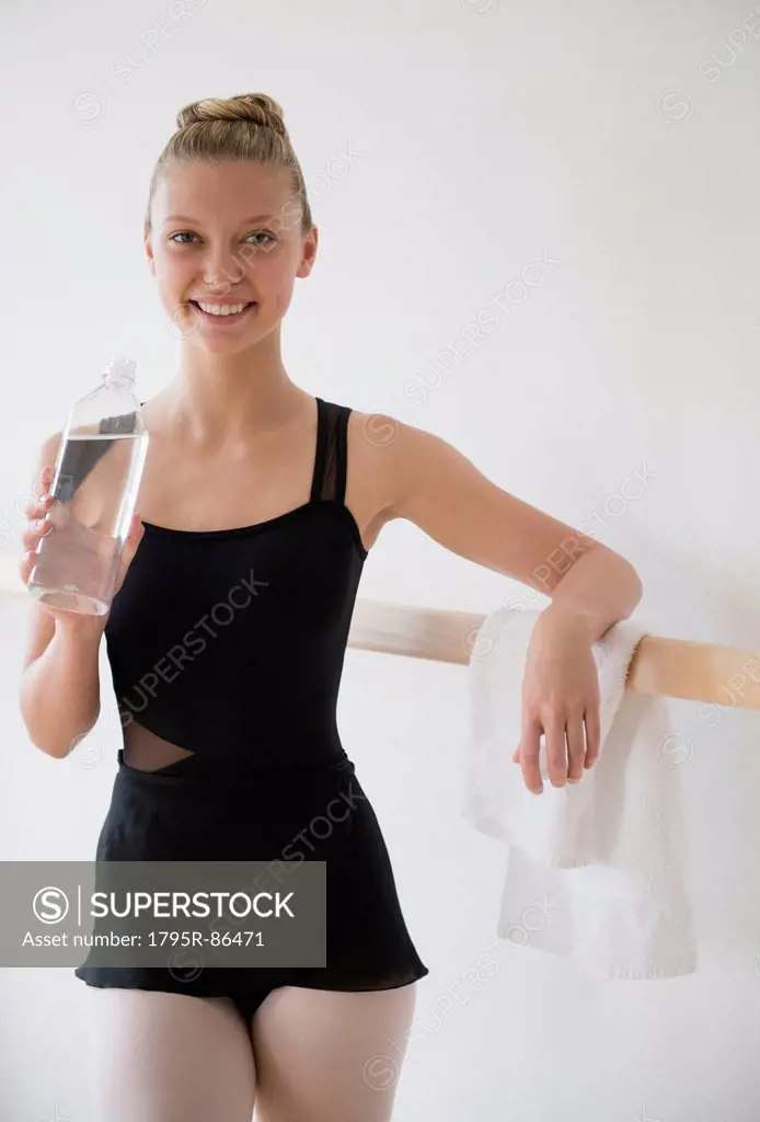 Portrait of teenage (16-17) ballet dancer standing at barre and holding water bottle