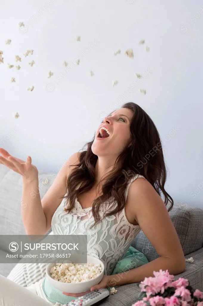 Young woman on sofa, throwing and catching popcorn