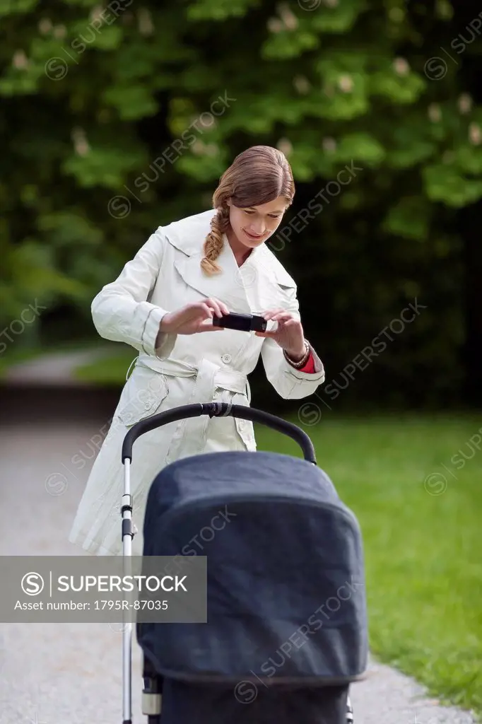 Mother with pram in park taking picture with cell phone