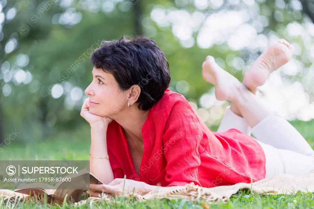 Mature woman lying on grass and reading book
