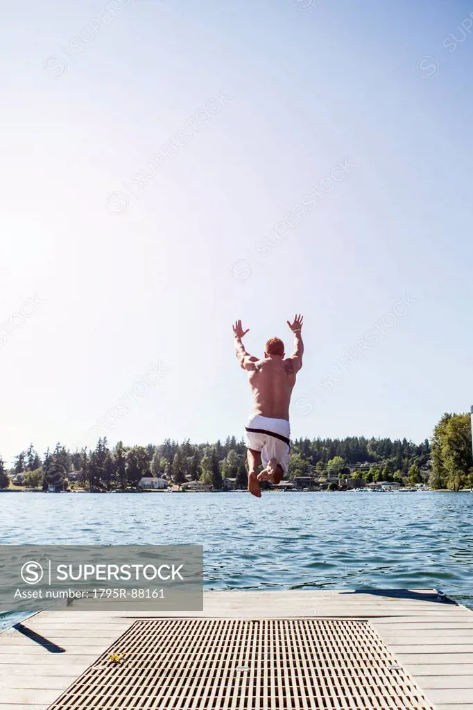 Young man jumping to lake from jetty