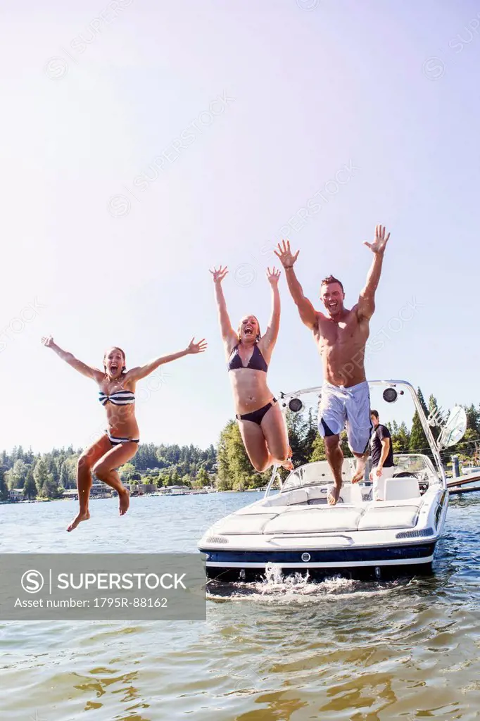 Young people jumping to lake from motorboat